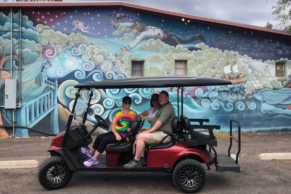 Group of three people on a golf cart tour in front of colorful street art in Bisbee, Arizona